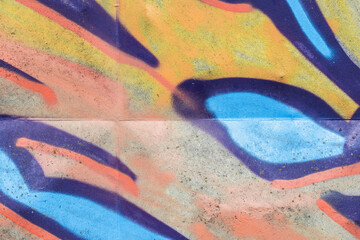 Bold, colorful graffiti mural sprayed on a concrete wall showing abstract shapes, vibrant blues and oranges, rough texture and layered paint. Urban street art composition conveying energy and creative © evannovostro