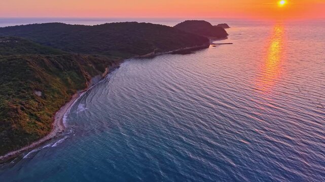 High-angle drone footage capturing a lush green pine forest meeting the crystal-clear turquoise waters of a secluded bay cape of Rodon(Kepi Rodonit), on beatiful sunset