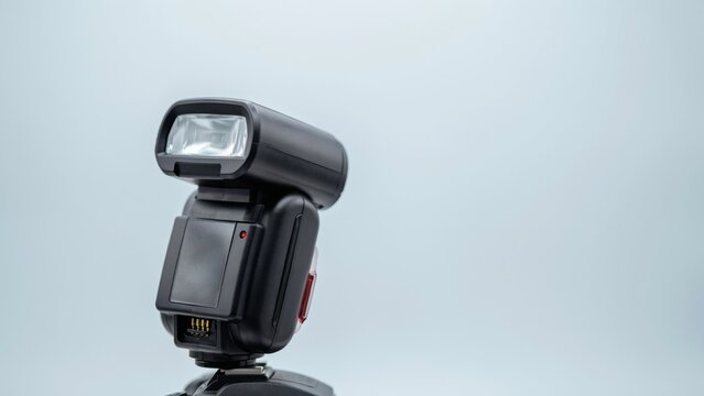 Professional external camera flash unit isolated against minimalist light gray studio background surface area with positioned against clean displays compact black