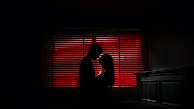 Silhouette of a romantic couple embracing against a vibrant red window blind, perfect for dating apps, romantic advertising and lifestyle branding