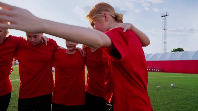 Young womens soccer team forming a pregame huddle on the training field, linking arms in bright red jerseys and building unity, focus, and motivation together