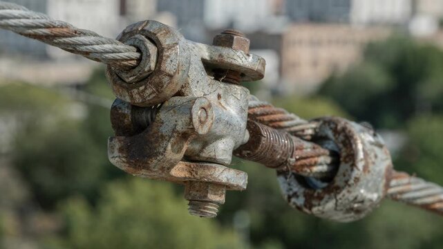 Detailed image of weathered guy wire connectors clear and sharp against an indistinct backdrop of mixed urban and green landscape.