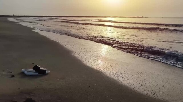 Pair of flip flops resting on golden beach sand at the shoreline as gentle waves repeatedly move in and out, with sea foam softly washing around the footwear, representing summer vacations