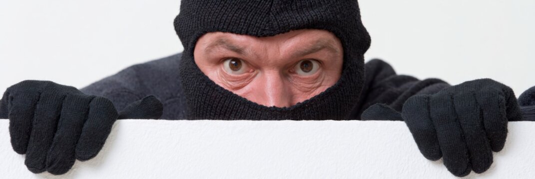 Masked intruder peering over blank white panel on isolated background