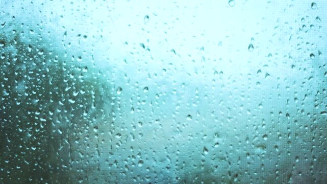 The scene shows water droplets on a glass pane, with rain creating a misty view. Rain blurs the outside landscape, enhancing the rainy atmosphere.