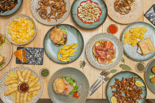 Overhead Restaurant Table: Ham Toast, Burgers, Fried Squid, Cheese Fries, Sandwiches and Spices Around Wooden Table