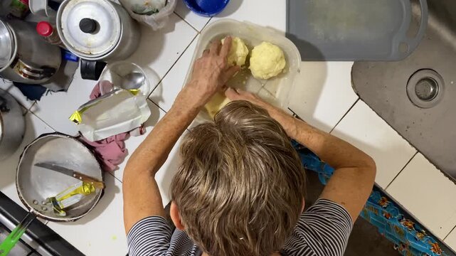 An elderly Colombian woman is kneading corn flour to prepare arepas for breakfast for her family in a kitchen in Neiva, Huila, Colombia. Concept of Colombian food