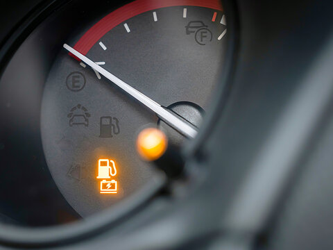 Close-up of a vehicle fuel gauge pointing to empty with a glowing low fuel warning light on the dashboard