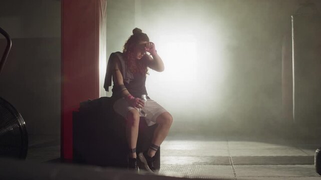 Young Caucasian woman walking, sitting on box, wiping sweat and drinking water in boxing gym, slow motion. Footage perfect for fitness advertisements and motivational sports campaigns