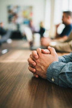 Close-up of hands clasped together on a wooden table