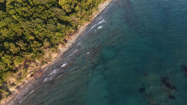 Overhead aerial view of a secluded beach, submerged rocks and forested coastline at Kepi i Rodonit, Albania.