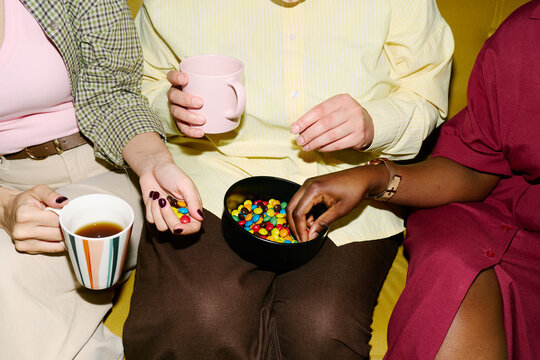 Close up of diverse women sharing candy and drinking tea while sitting together, showing casual friendship and social bonding. Ideal for lifestyle marketing, community campaigns
