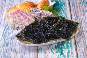 Nori seaweed sheets on ceramic plate with seashells and oyster on weathered wood © Andrei Starostin