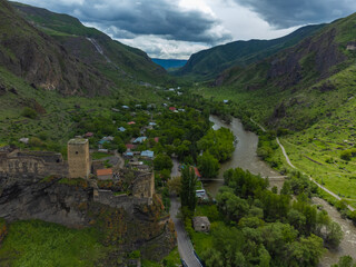 Khertvisi fortress, a medieval castle, stands on a rocky cliff overlooking the kura river winding through a lush green valley and small village in georgia's caucasus mountains © yaroslav1986