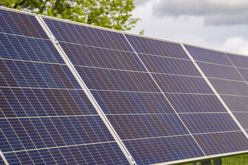 Obraz premium Solar panels stand in a vibrant green field with yellow dandelions, collecting clean energy from the sun on a partially cloudy day, symbolizing renewable power and environmental protection