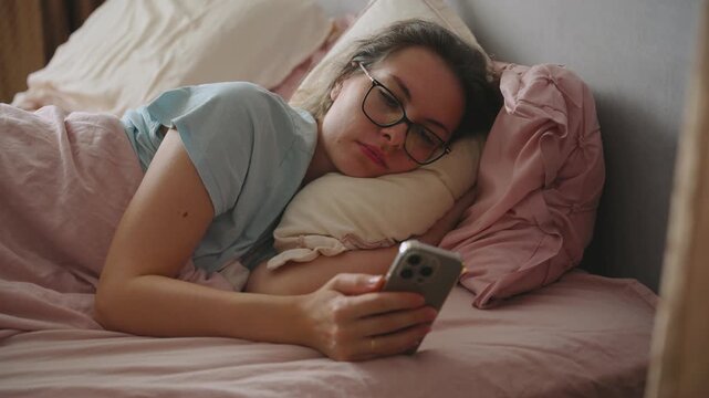 sad unhappy depressed woman lies in bed holding phone scrolling through news feed, reading book online. Upset lonely girl suffering from insomnia. Concept sorrow frustrated headash problems stress