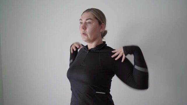 Focused exerciser does standing dynamic shoulder shrugs with hands on upper chest to loosen neck and upper back before a workout.