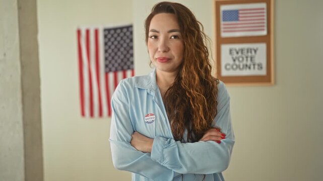 Woman wearing a voted sticker with arms crossed in a polling building beside an american flag and an every vote counts poster; pride civic duty.
