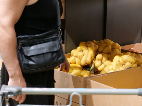 Man selecting fresh bagged potatoes from cardboard bins inside a grocery store or supermarket.