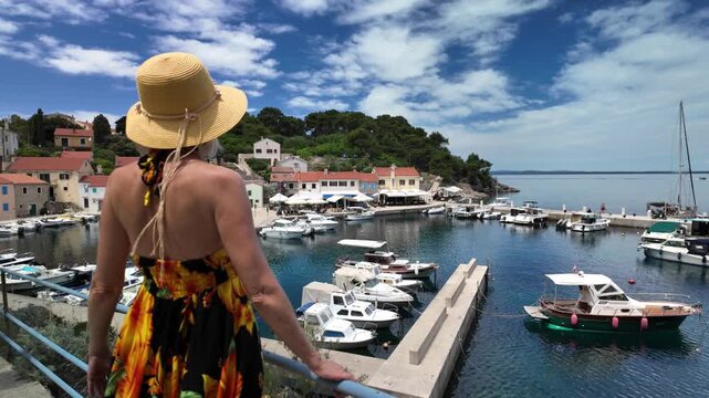 Woman enjoying a summer day, on a vibrant boardwalk in Luka Rovenska harbor surrounded by colorful traditional houses and boats on Losinj Island, Croatia