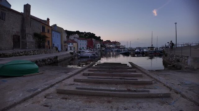 Coastal village harbor vibrant with evening lights, reflecting colorful houses and numerous boats in clear, calm water, highlighting charm of Rovenska, Mali Losinj, Croatia of Losinj Island in Croatia