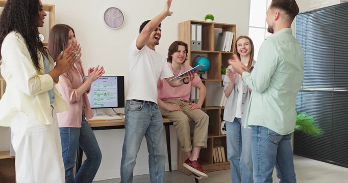 Students team meeting shows collaboration and success. A diverse group in a bright office applauds with high fives after a project win near computers. Clear concept teamwork success and unity.