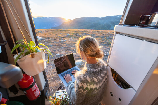 Woman working on laptop inside camper van during golden hour with mountain adventure lifestyle technology computer
