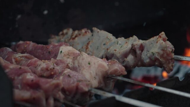 Fresh marinated meat grilling on metal skewers over hot charcoal and open flame
