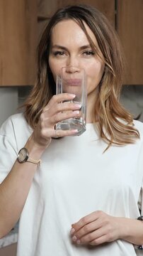 Beautiful young woman drinking pure fresh water from a glass to stay hydrated and healthy, promoting a wellness lifestyle, and then looking at the camera with a cheerful smile