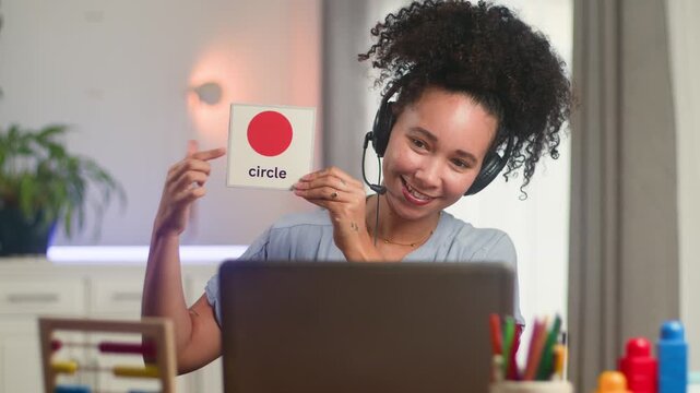 Smiling Black Woman Online Teacher Remotely Teaches Shapes with Flashcards for Early Education