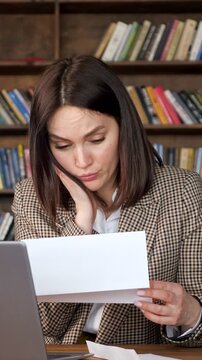 Frustrated businesswoman sitting at her desk, opening an envelope and reading a letter with bad news, her expression shifting from curiosity to shock, disappointment, and despair