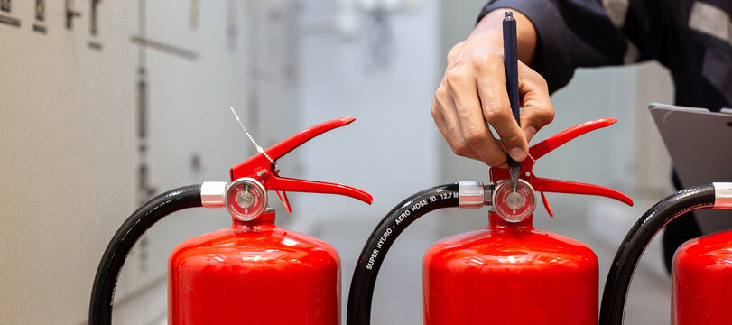 Technician engineer checking pressure gauge of fire extinguisher with pen for annual safety inspection in factory.