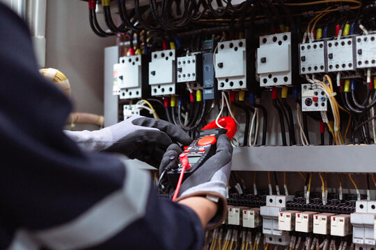 Electrician using digital clamp meter to measure electrical current in control panel.