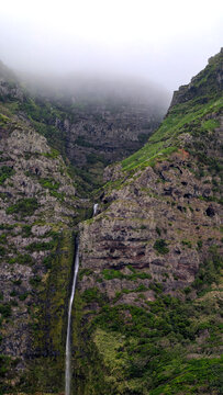 Waterfall streams down steep volcanic cliff surrounded by mountain fog on Faja Grande, Flores, Azores islands. 
