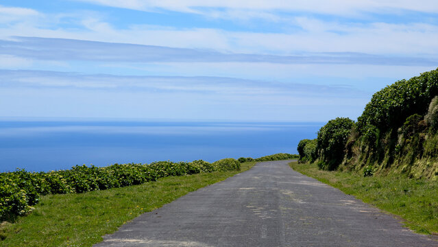 Scenic coastal road stretches along green hills toward vast blue ocean waters on Corvo island, Azores, Portugal.