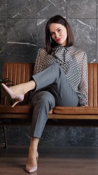 Confident businesswoman with a short haircut sitting gracefully on a brown leather bench in a contemporary office space, posing for the camera with a self assured and professional demeanor