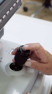 Close up of an optometrist's hand expertly maneuvering the joystick of a modern autorefractor, performing a detailed vision exam to accurately check a patient's eyesight