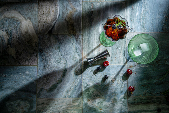 Craft cocktail with vintage tumbler, jigger and fresh berries on textured stone background