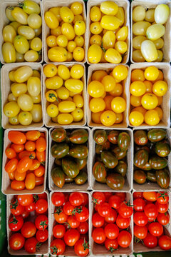 Fresh tomatoes of various colors displayed in paper baskets at a market