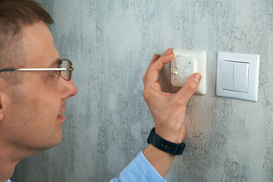 A man adjusting the central heating thermostat in her home