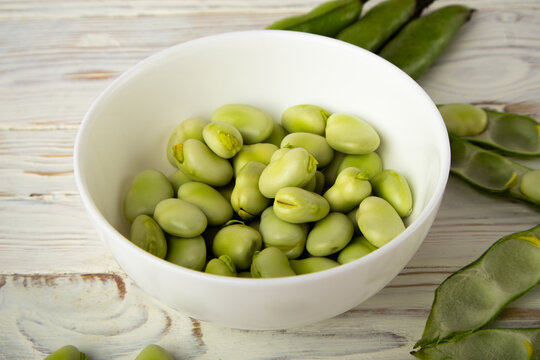 Fresh fava beans in white bowl on wooden table