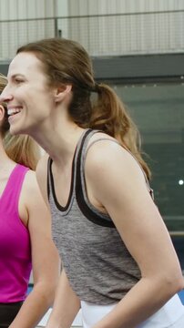 Vertical video: Smiling gray top woman leaning and touching teammate shoulder at blue court, net