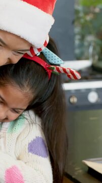 Vertical video: Guiding mom in Santa hat, daughter reaching for tray to bake in kitchen