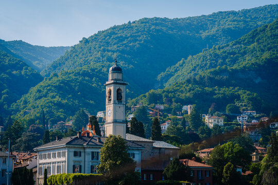 Scenic view of Carate Urio with historic clock tower and lush green mountains in the background, Italy's natural beauty on display