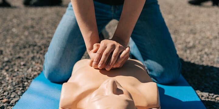 Hands On Outdoor CPR Training Session Demonstrating Life Saving Chest Compressions On A Medical Manikin On A Blue Mat For Emergency Preparedness And First Aid Education
