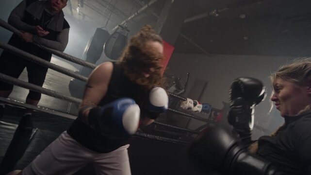 Caucasian young women sparring in boxing ring during training session with Caucasian male coach watching. Ideal for fitness brand commercials and women empowerment campaigns