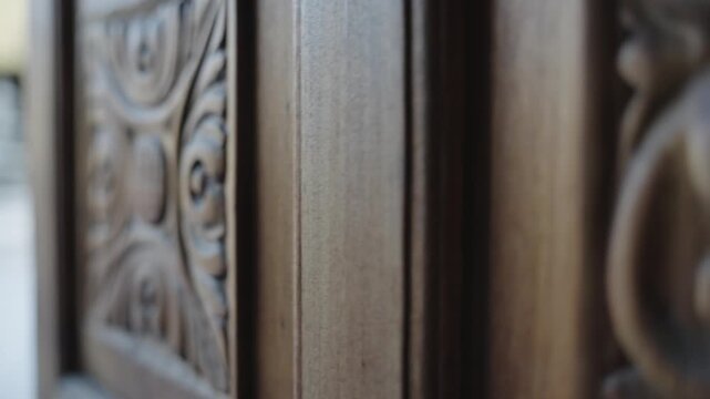 Close up view of a hand carved wooden door with intricate floral patterns revealing a courtyard