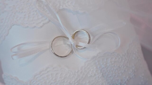 Close Up of Gold Wedding Rings Tied with White Ribbon on Ring Pillow