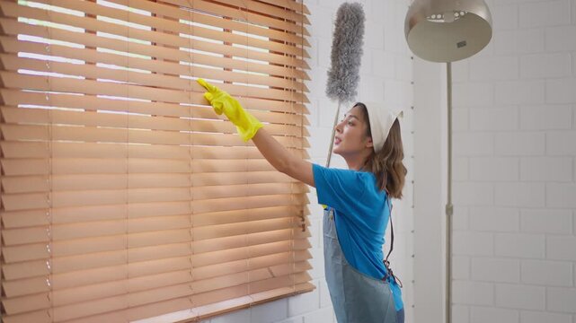 Cleaning woman blind window glove duster home housework wooden cleaner wiping dust near bright interior window with yellow glove apron focused housekeeping dust removal