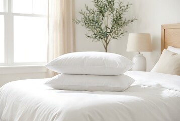 Fototapeta premium Two white fluffy pillows stacked neatly on tidy unmade bed with soft linen bedding in bright bedroom showing interior design concept with blurred olive tree and bedside lamp behind.